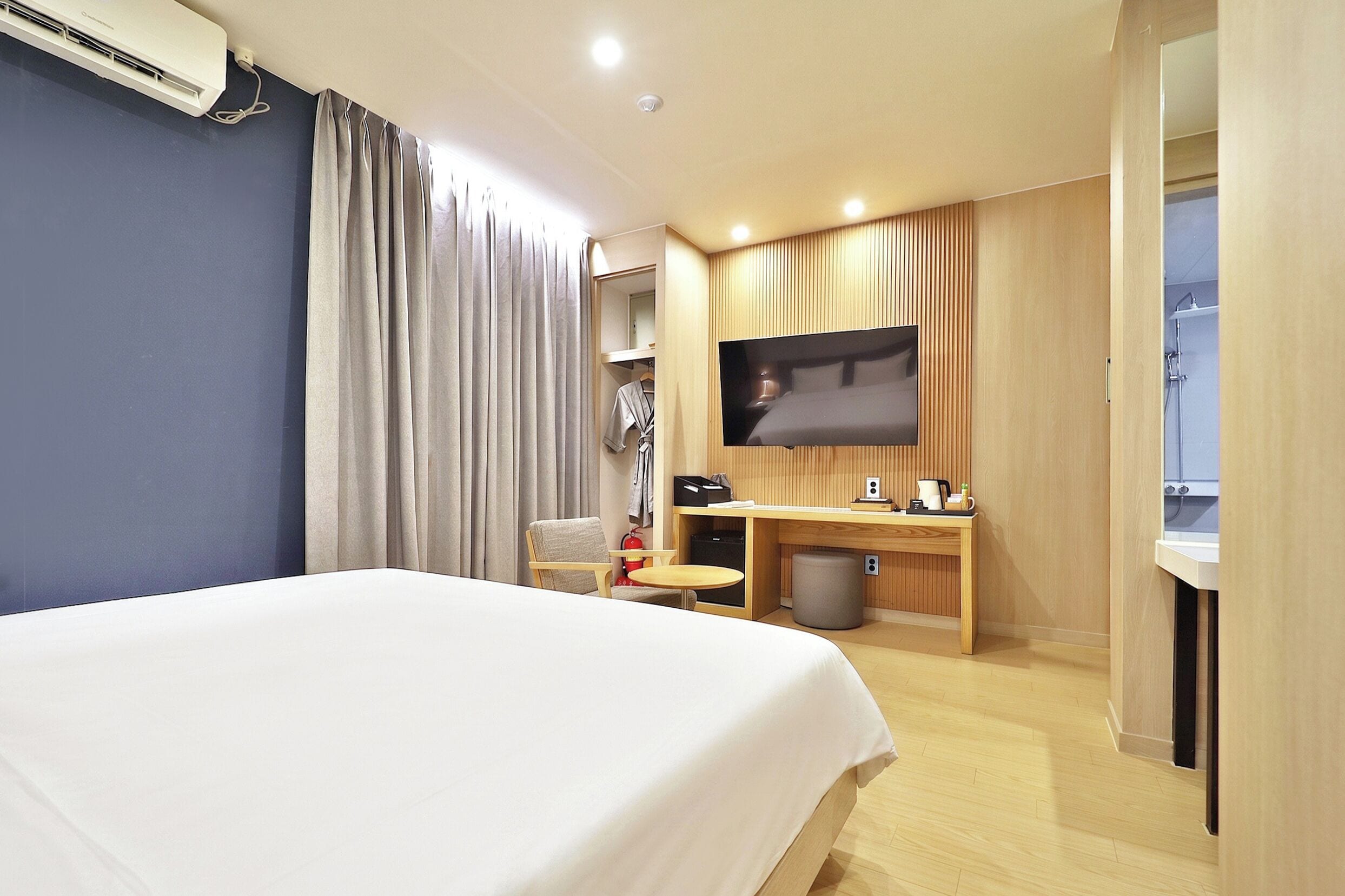 Habitación de hotel con cama, escritorio, televisor y zona de ducha.
