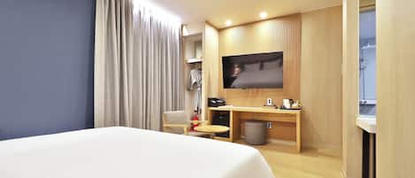 Habitación de hotel con cama, escritorio, televisor y zona de ducha.