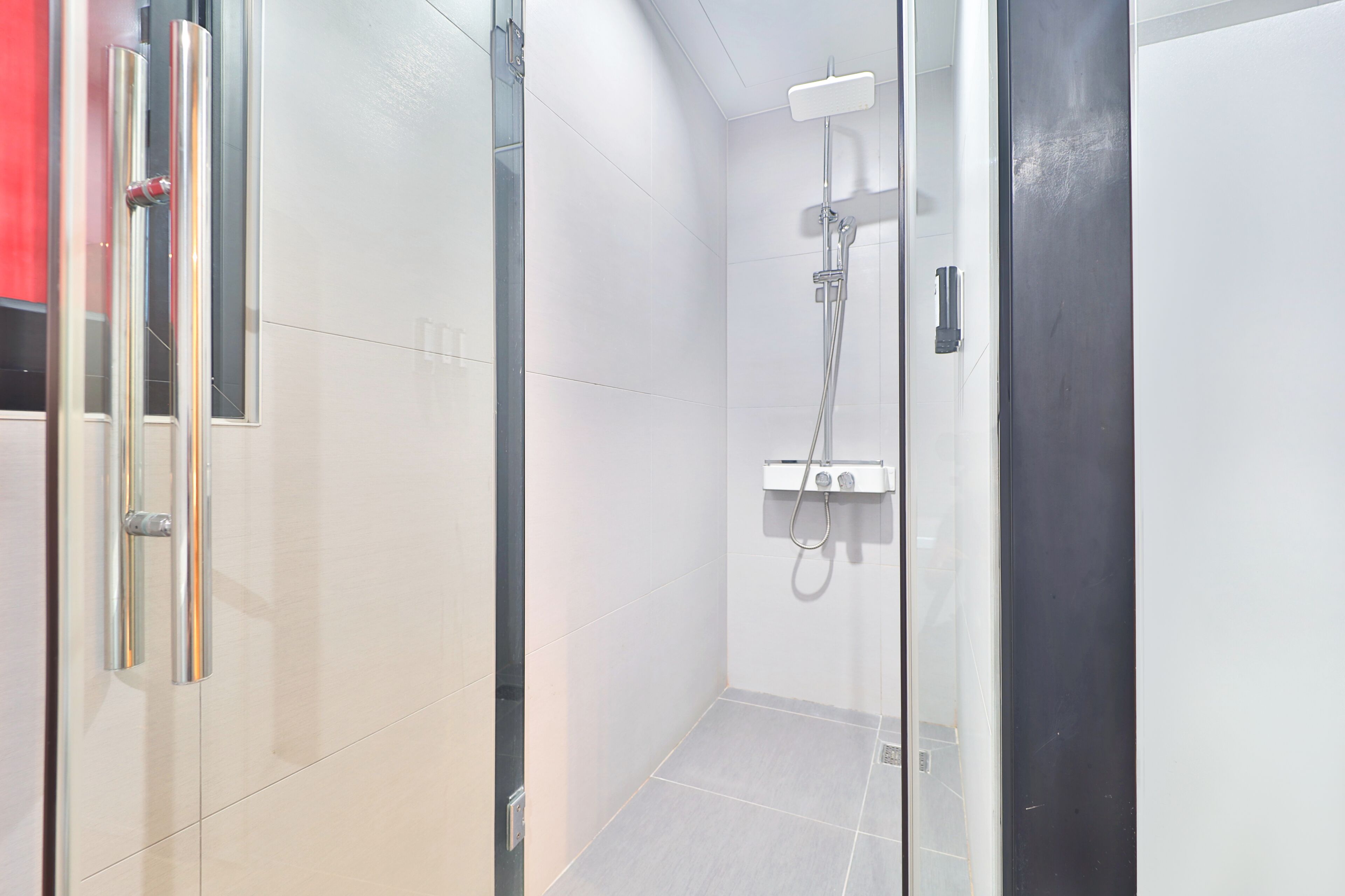 A modern bathroom with a glass shower enclosure, a white tiled wall, and a door with a metallic handle.