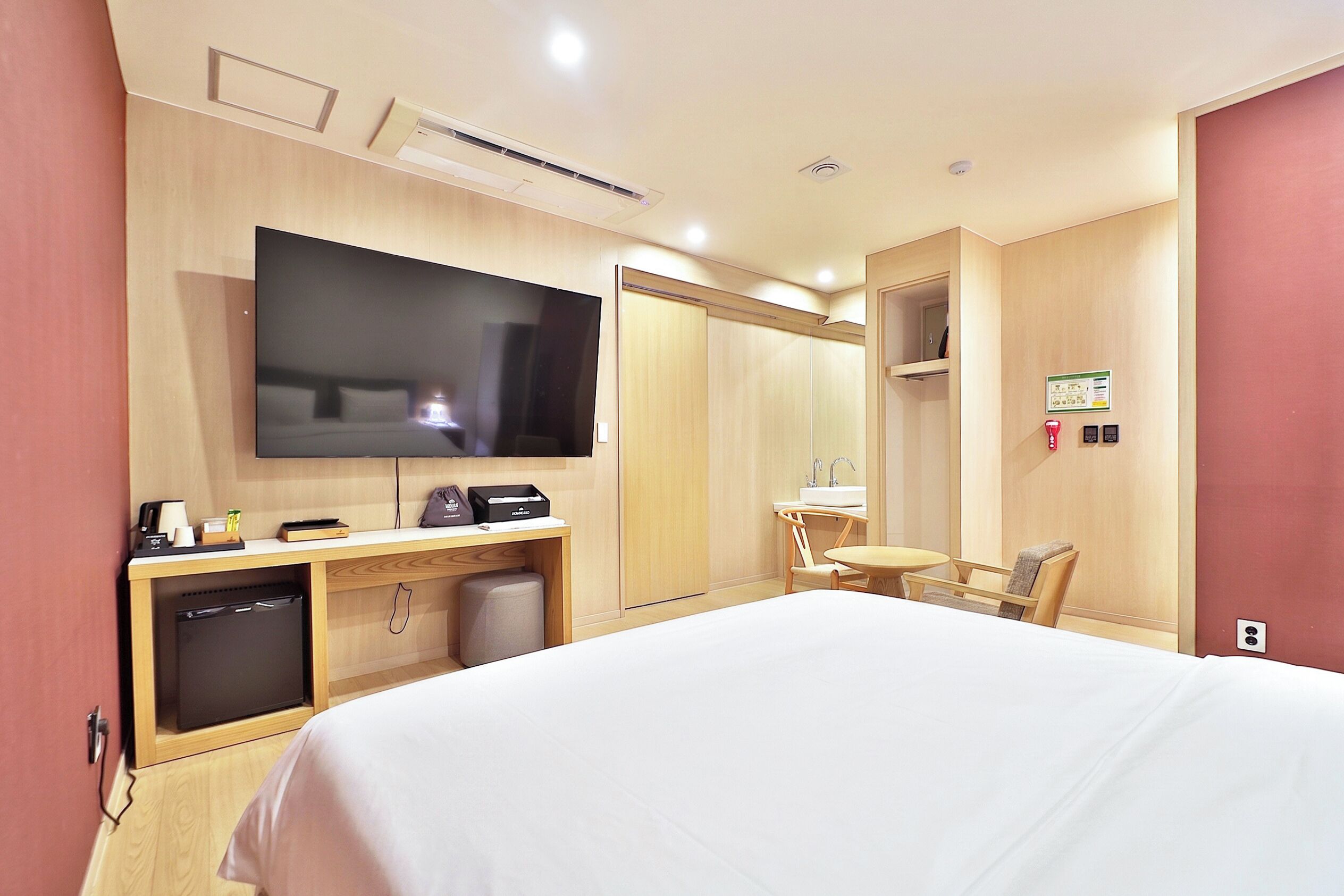 Quarto de hotel com cama, televisão, escrivaninha com computador, cadeira e mesa pequena.