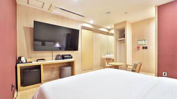 Quarto de hotel com cama, televisão, escrivaninha com computador, cadeira e mesa pequena.