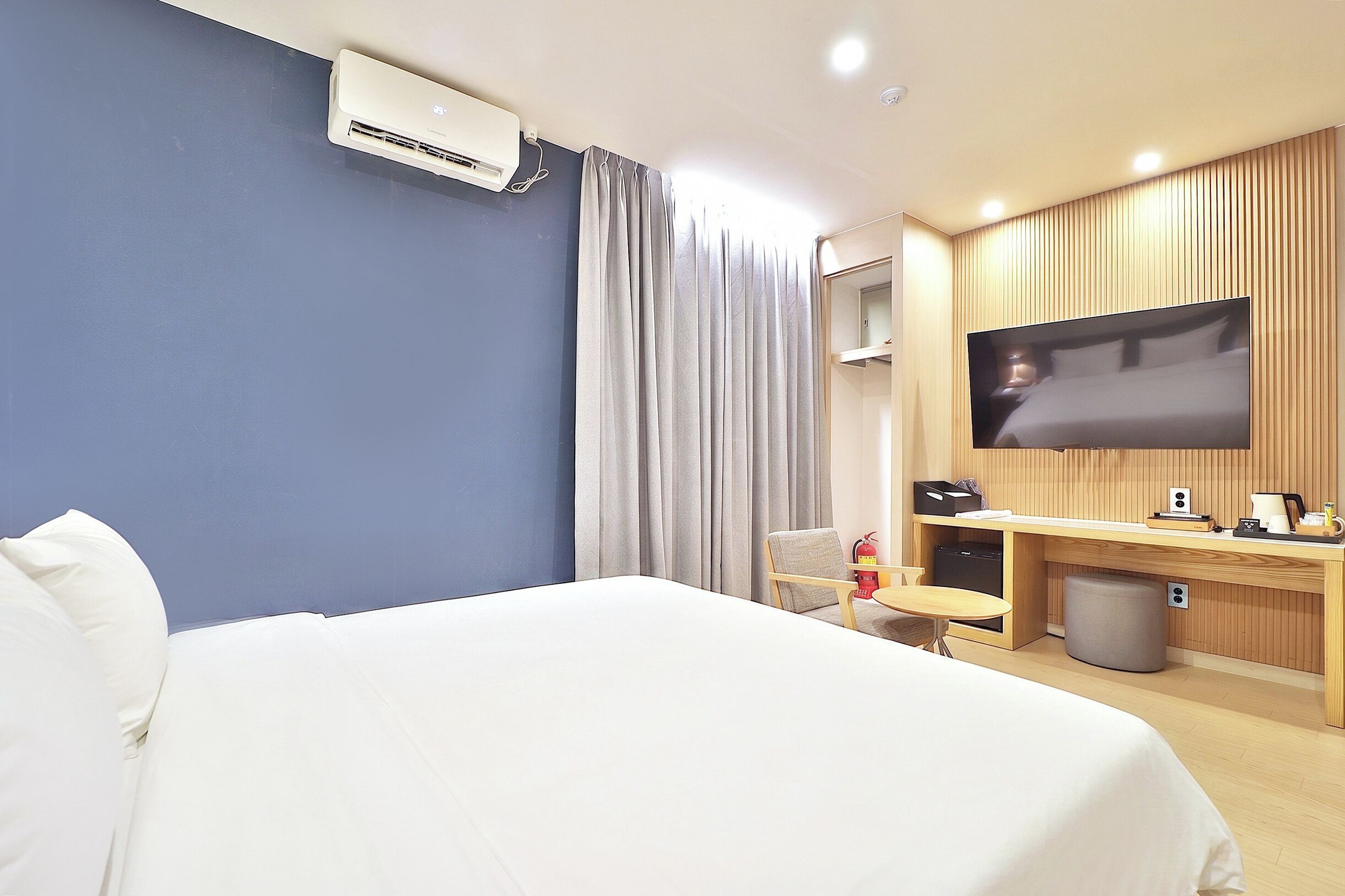 Une chambre d’hôtel comprenant un lit, un bureau avec un téléviseur à écran plat, une chaise, une poubelle et un extincteur.