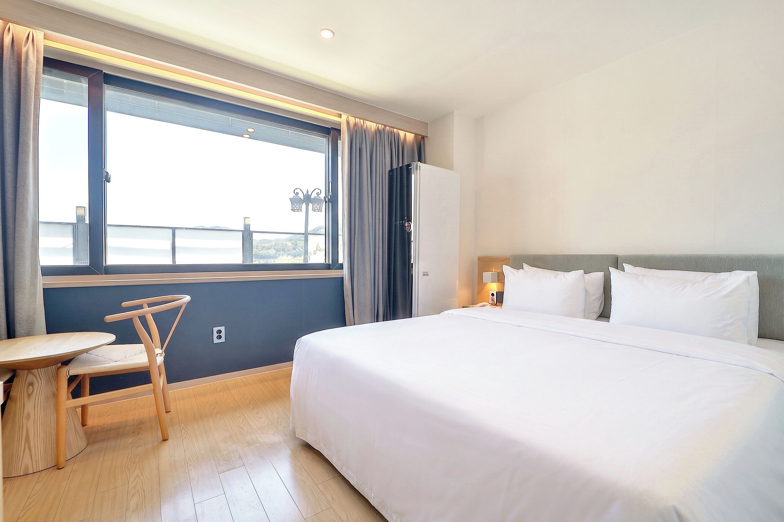 A hotel room with a large bed, a desk, a chair, a window with curtains, and a view of the sea.