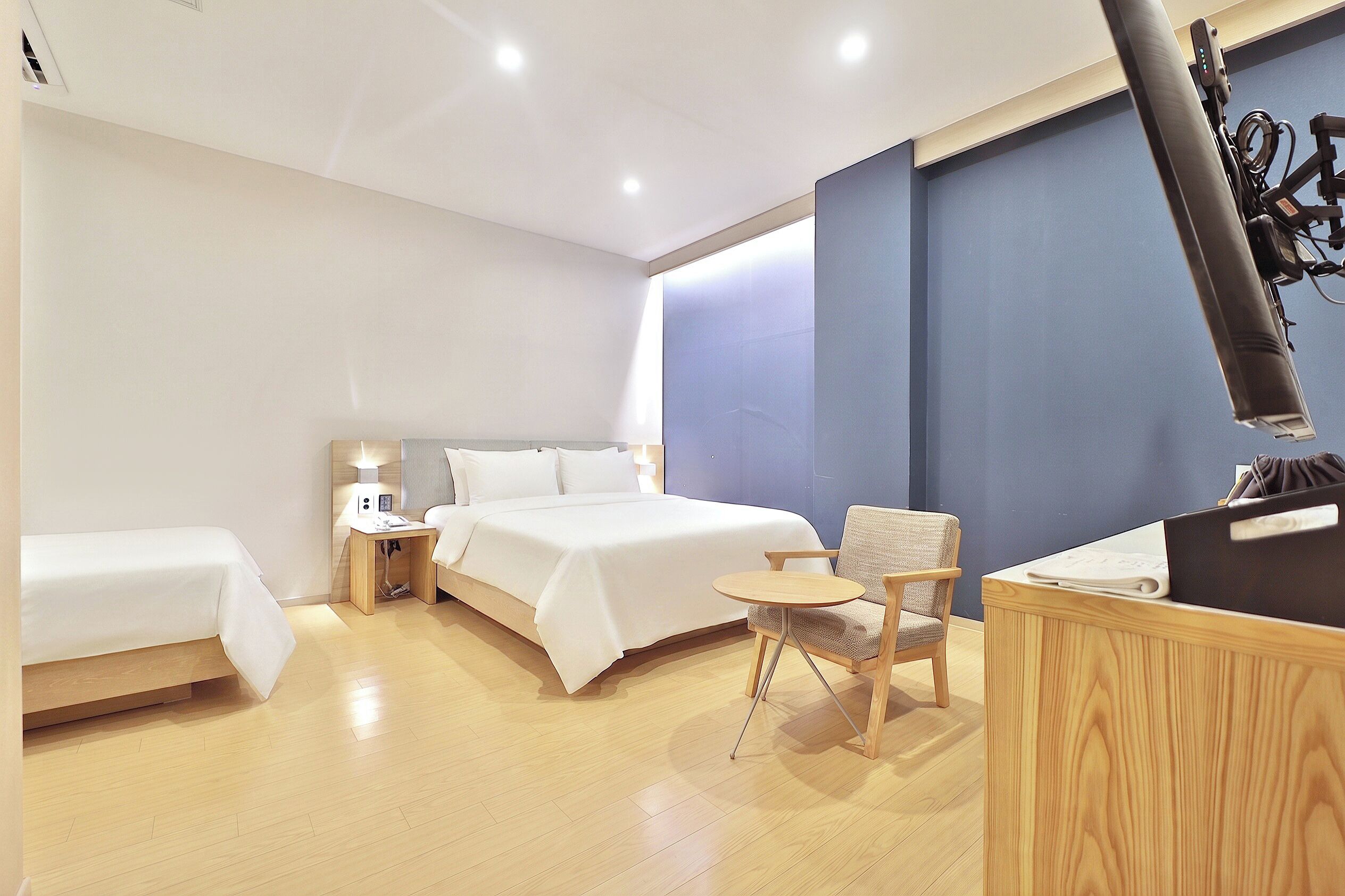 A hotel room with a bed, bedside table, chair, and a desk with a television.