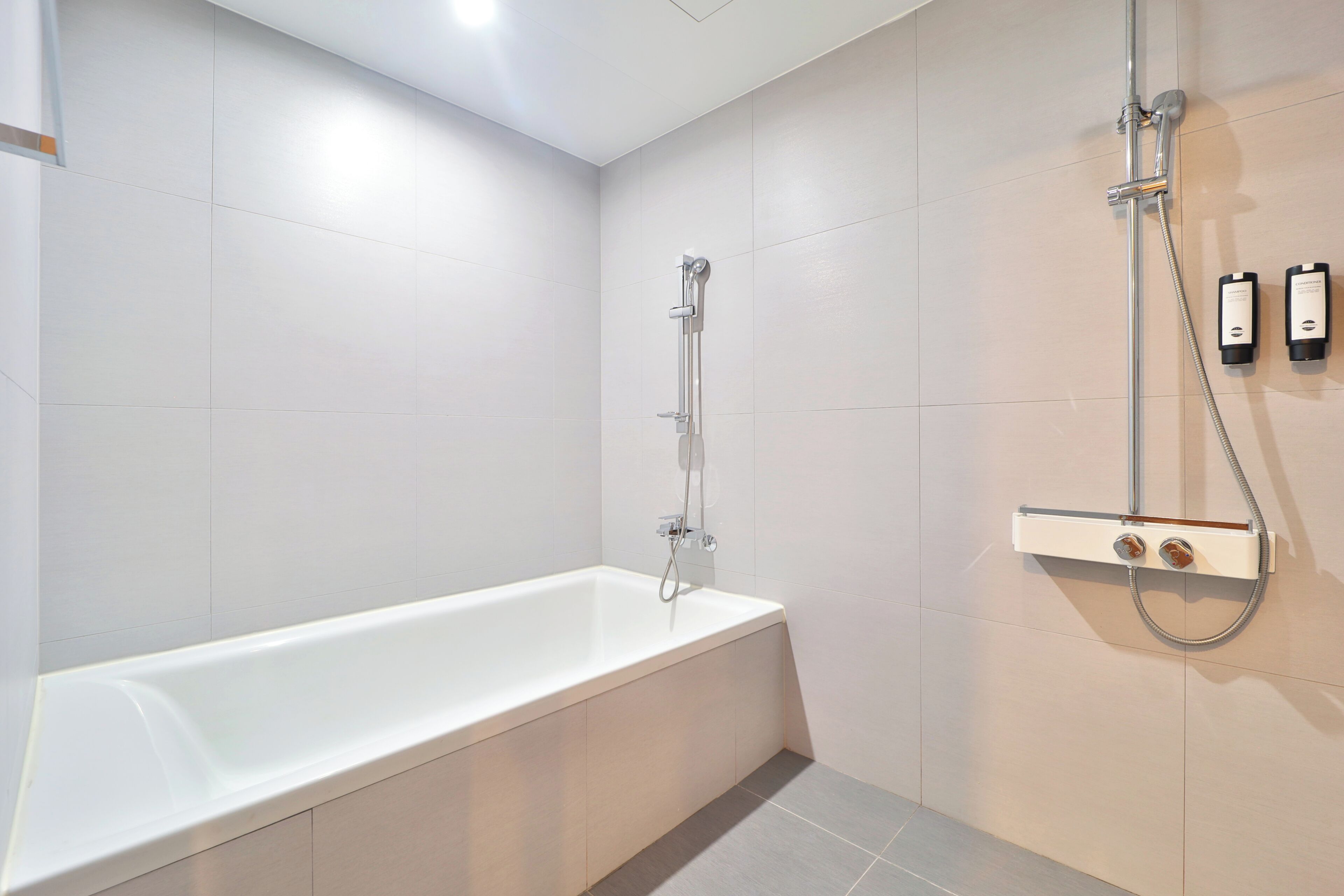 A modern bathroom with a white bathtub, a shower unit, and two bottles of shampoo and conditioner.