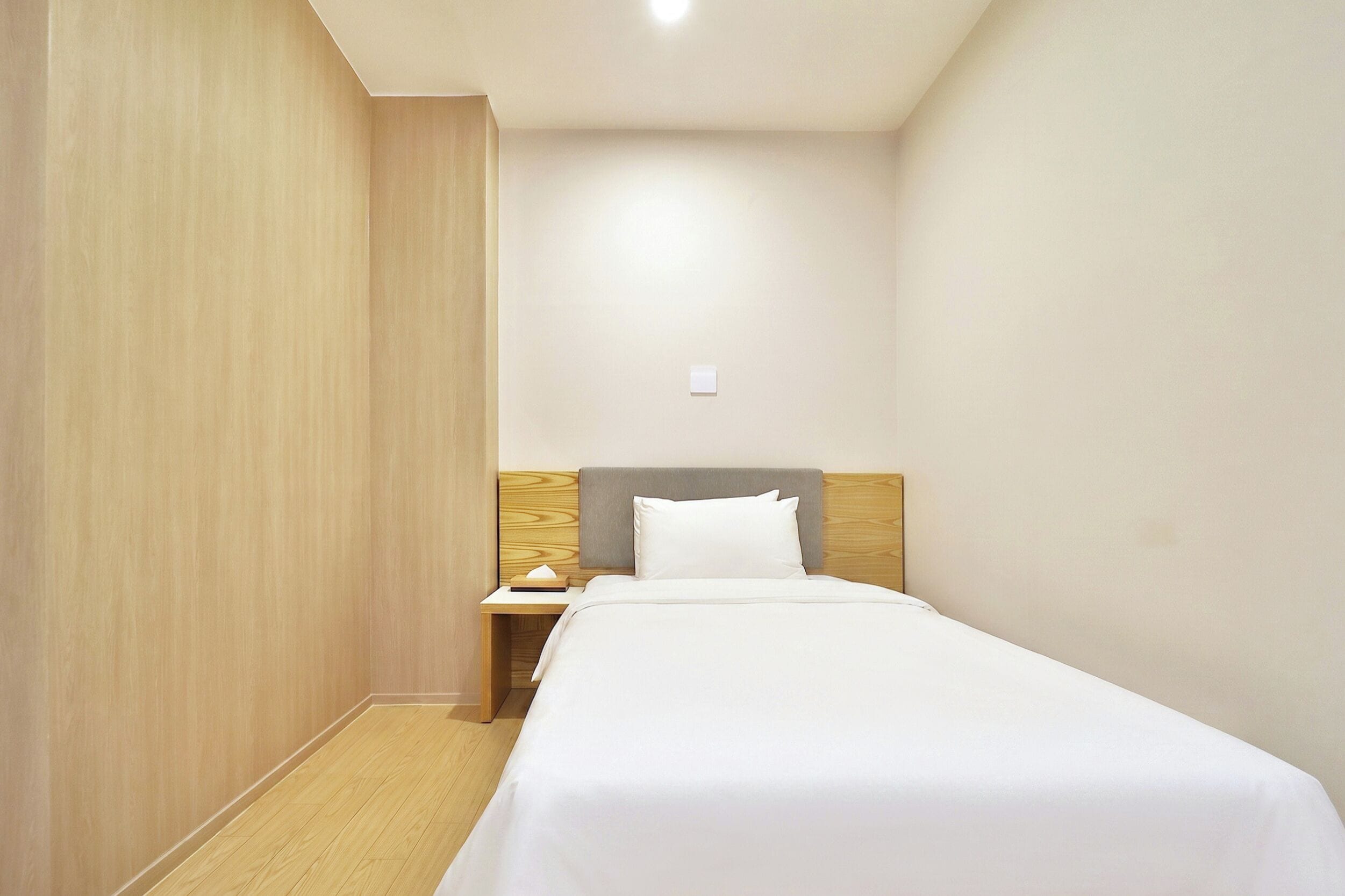 Una cama individual con cabecera de madera y una mesita de noche con lámpara, en una habitación con paredes y suelo de madera.