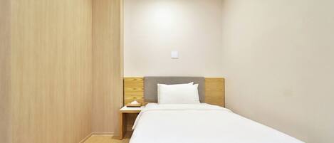 Una cama individual con cabecera de madera y una mesita de noche con lámpara, en una habitación con paredes y suelo de madera.