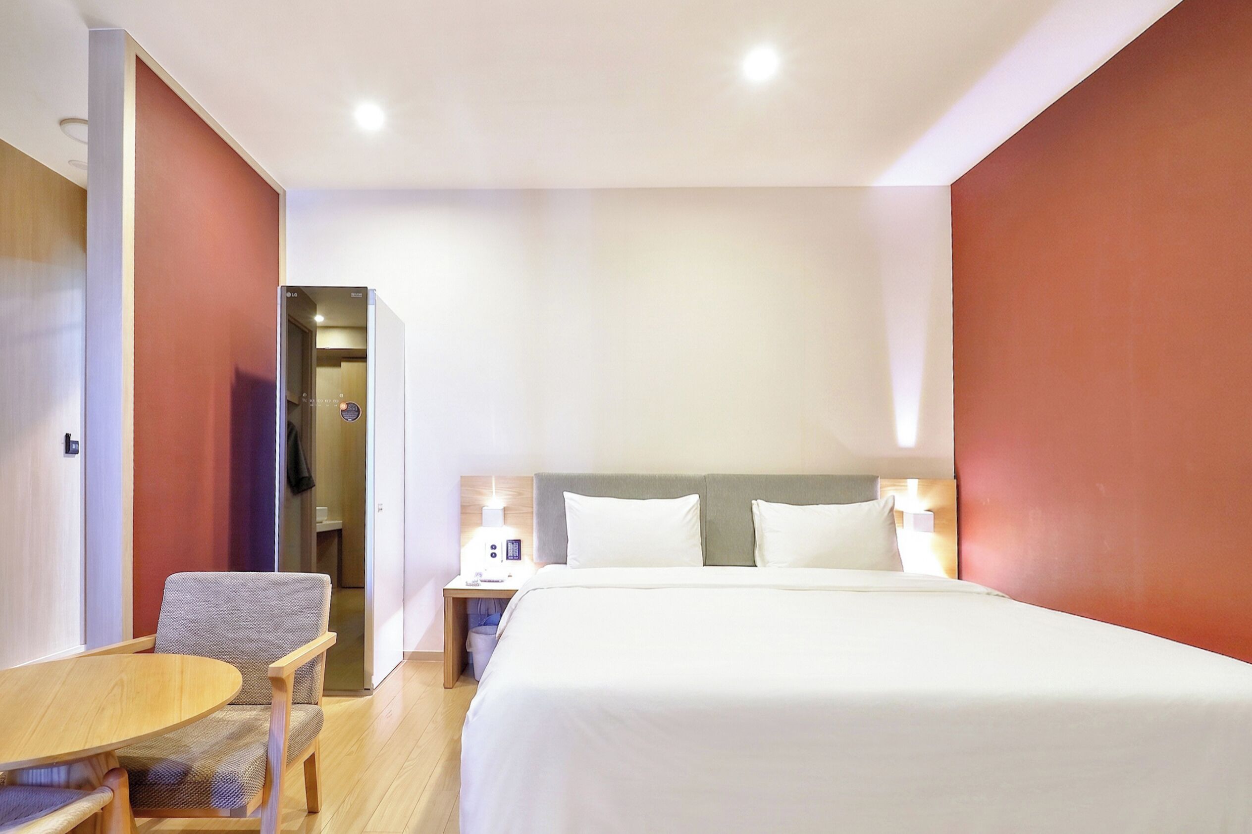 Una habitación de hotel con cama, mesita de noche, silla y una pequeña mesa con otra silla.