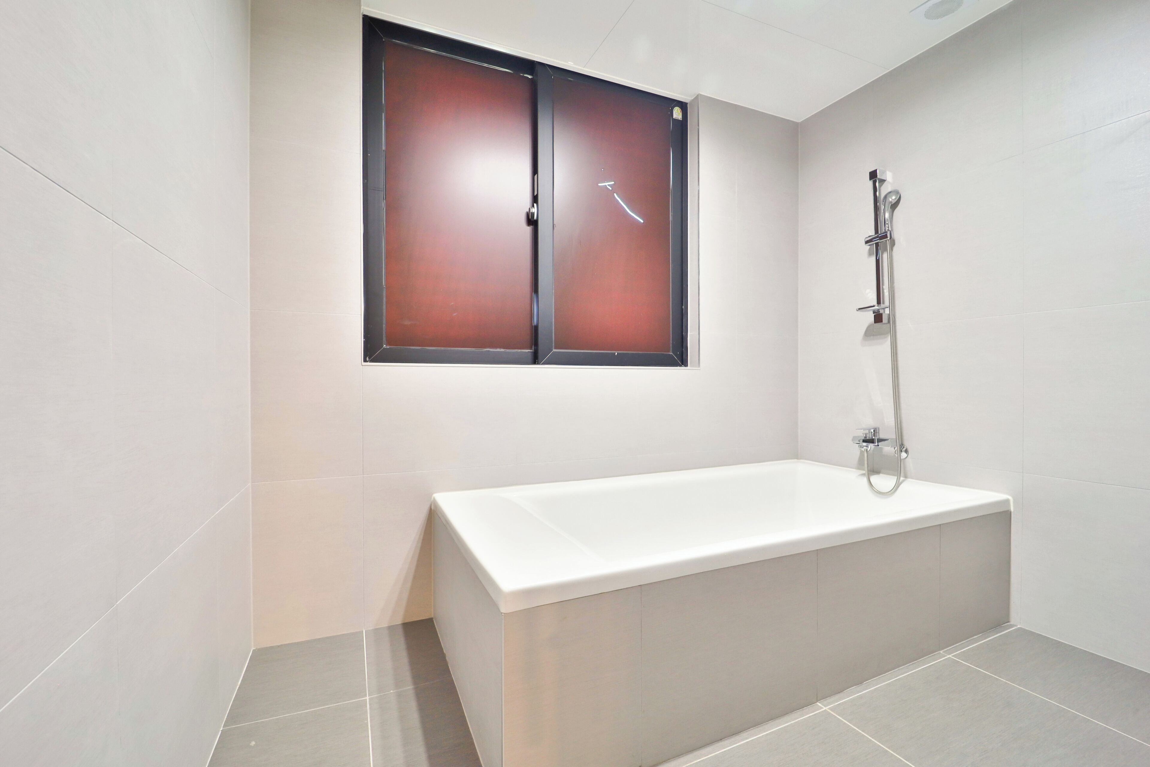 A modern bathroom with a white bathtub, a shower, and a window with a dark frame.