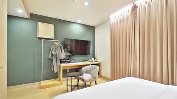 A hotel room with a bed, a desk with a chair, a television, and a wardrobe.