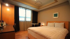 A hotel room with a bed, a desk, a chair, a small table, and a window with curtains. - Changwon AT Business Hotel (Changwon)