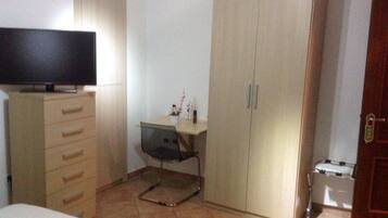 Un dormitorio con cama, cómoda, escritorio con silla, armario y televisor sobre la cómoda.