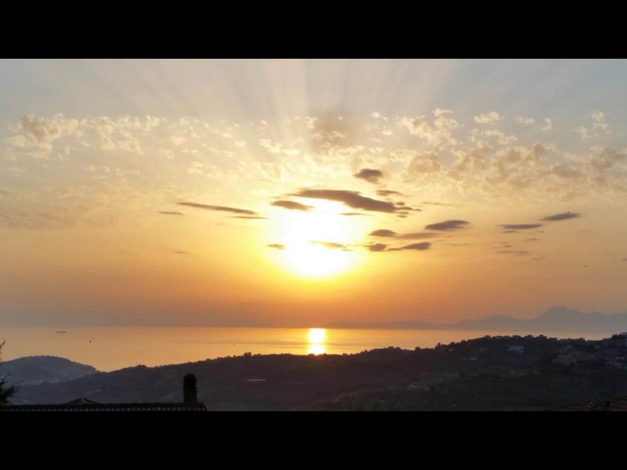 Tramonto su un paesaggio collinare con la sagoma di un edificio in primo piano.