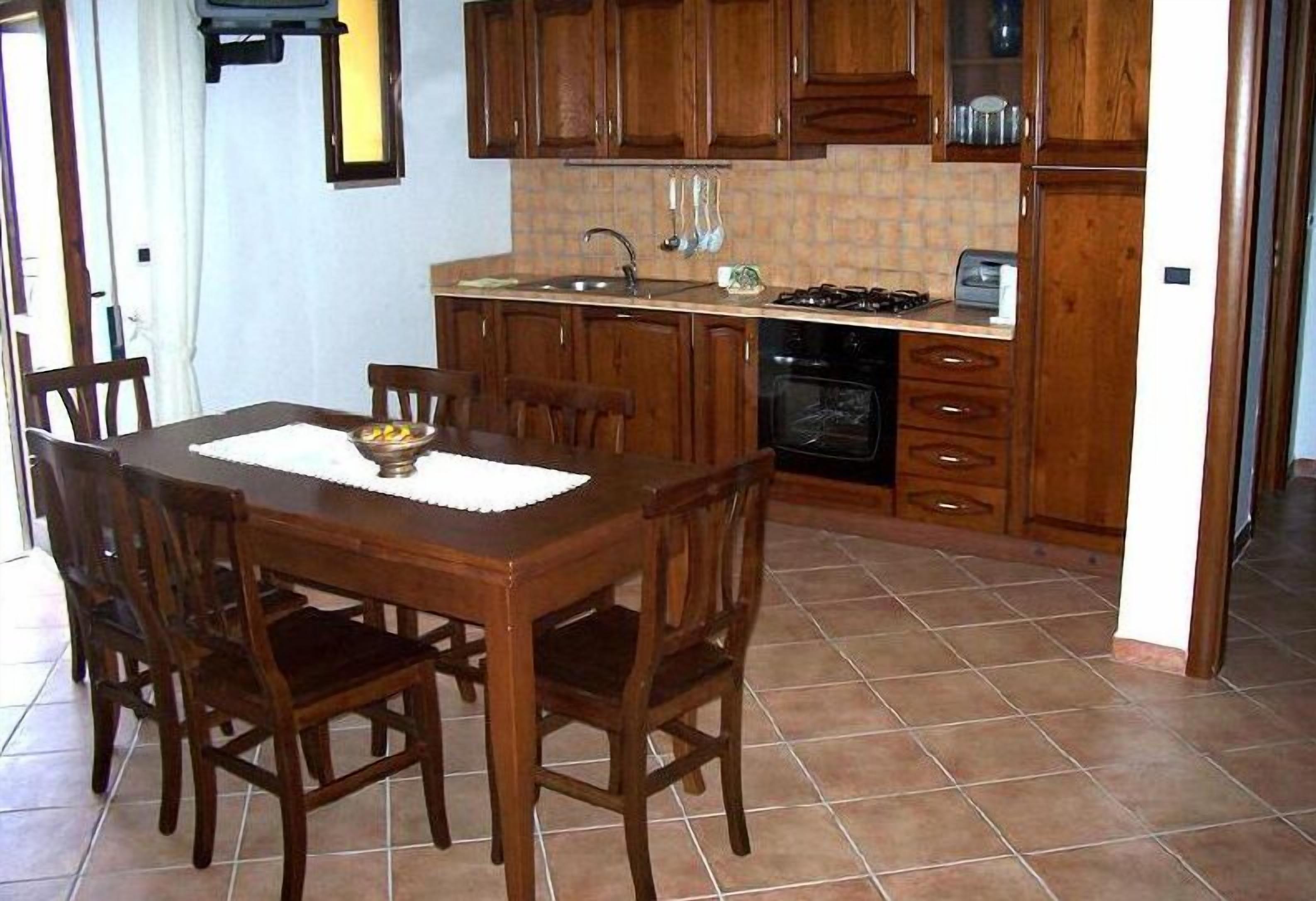 Une cuisine avec des meubles de rangement en bois, une table à manger avec des chaises, une cuisinière et un évier.