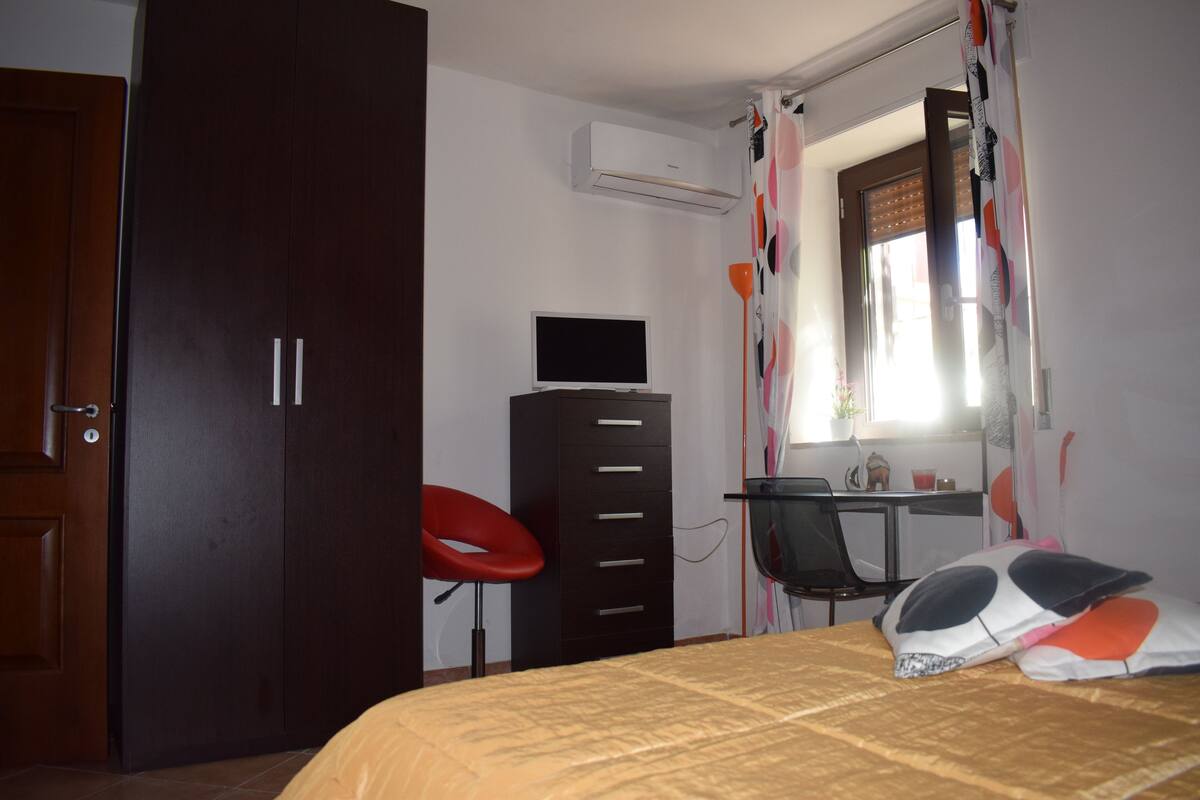 Ein Schlafzimmer mit Bett, Schreibtisch, Stuhl, Kleiderschrank und Klimaanlage.