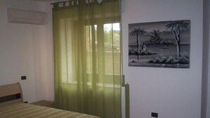 Ein Schlafzimmer mit einem Bett, einem Fenster mit durchsichtigen Vorhängen, einer Wand-Klimaanlage und einem Landschaftsbild.