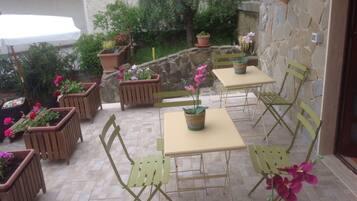 An outdoor patio with wooden chairs and tables, surrounded by potted plants and a stone wall.