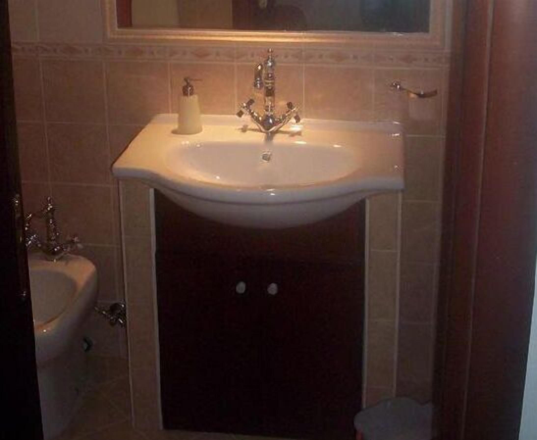 A bathroom with a white sink, a mirror above it, and a toilet to the left.