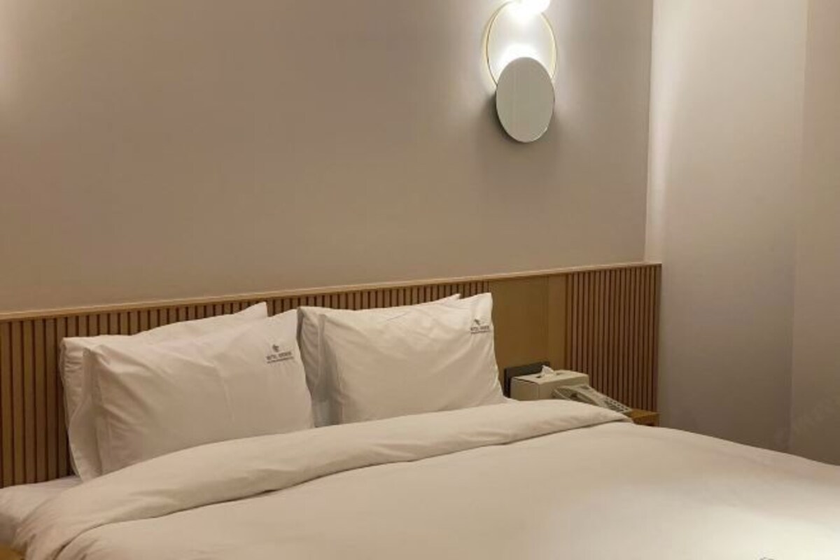 A hotel room with a neatly made bed, a bedside table with a lamp, and a wall-mounted light fixture.