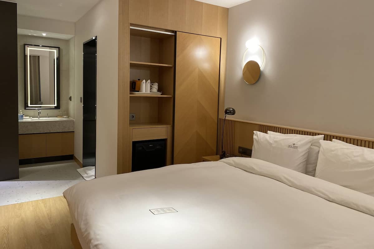 Habitación de hotel con cama, armario empotrado, tocador con espejo y mesita de noche.