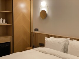 Una habitación de hotel con cama, mesita de noche, lámpara, espejo y armario.