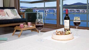 Et spiseområde med et bord dækket til to, inklusive en vinflaske, to glas og dessert. En sofa og et lille bord med kopper og kager ses i baggrunden.