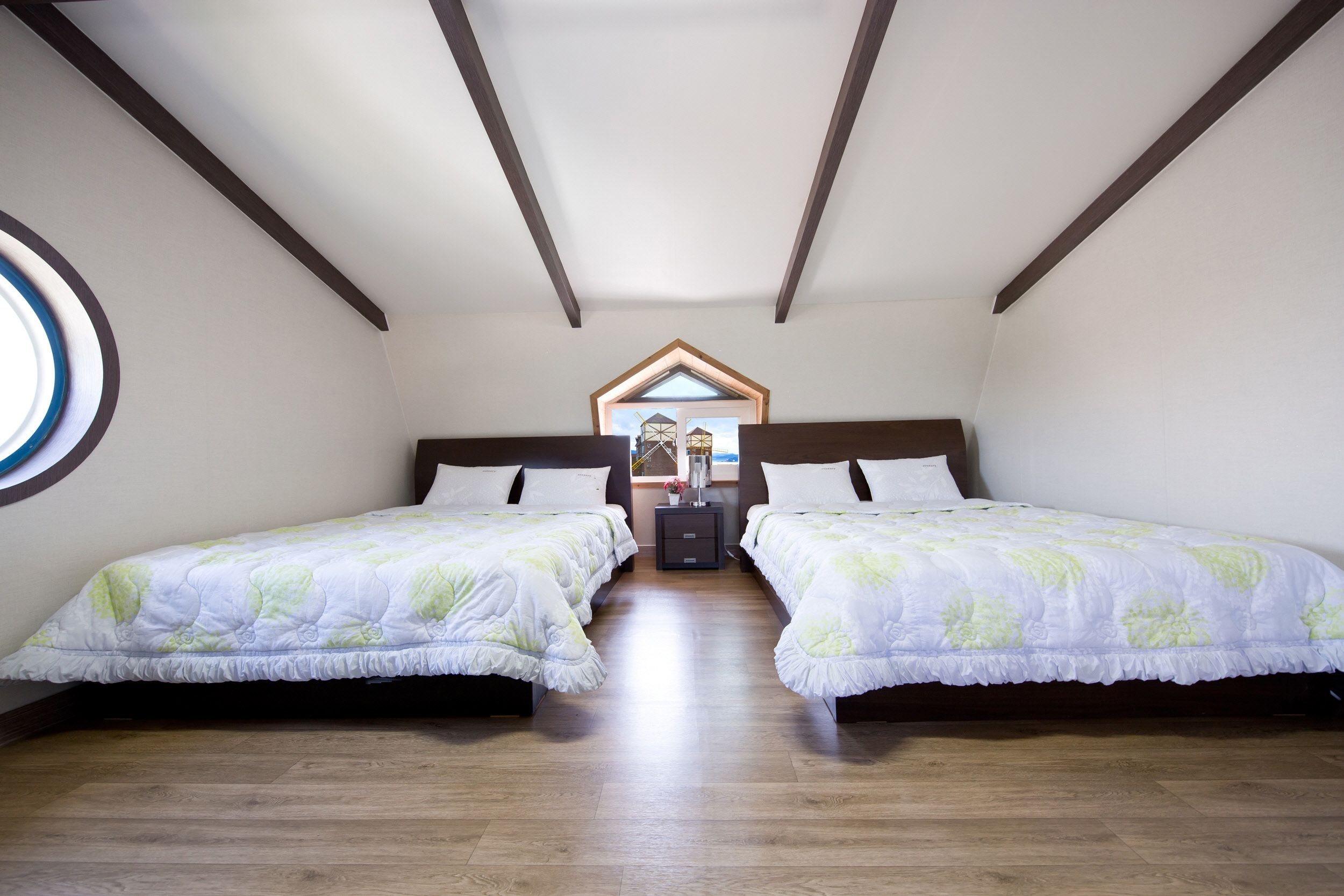 A bedroom with two beds, wooden flooring, a skylight, and a small window.