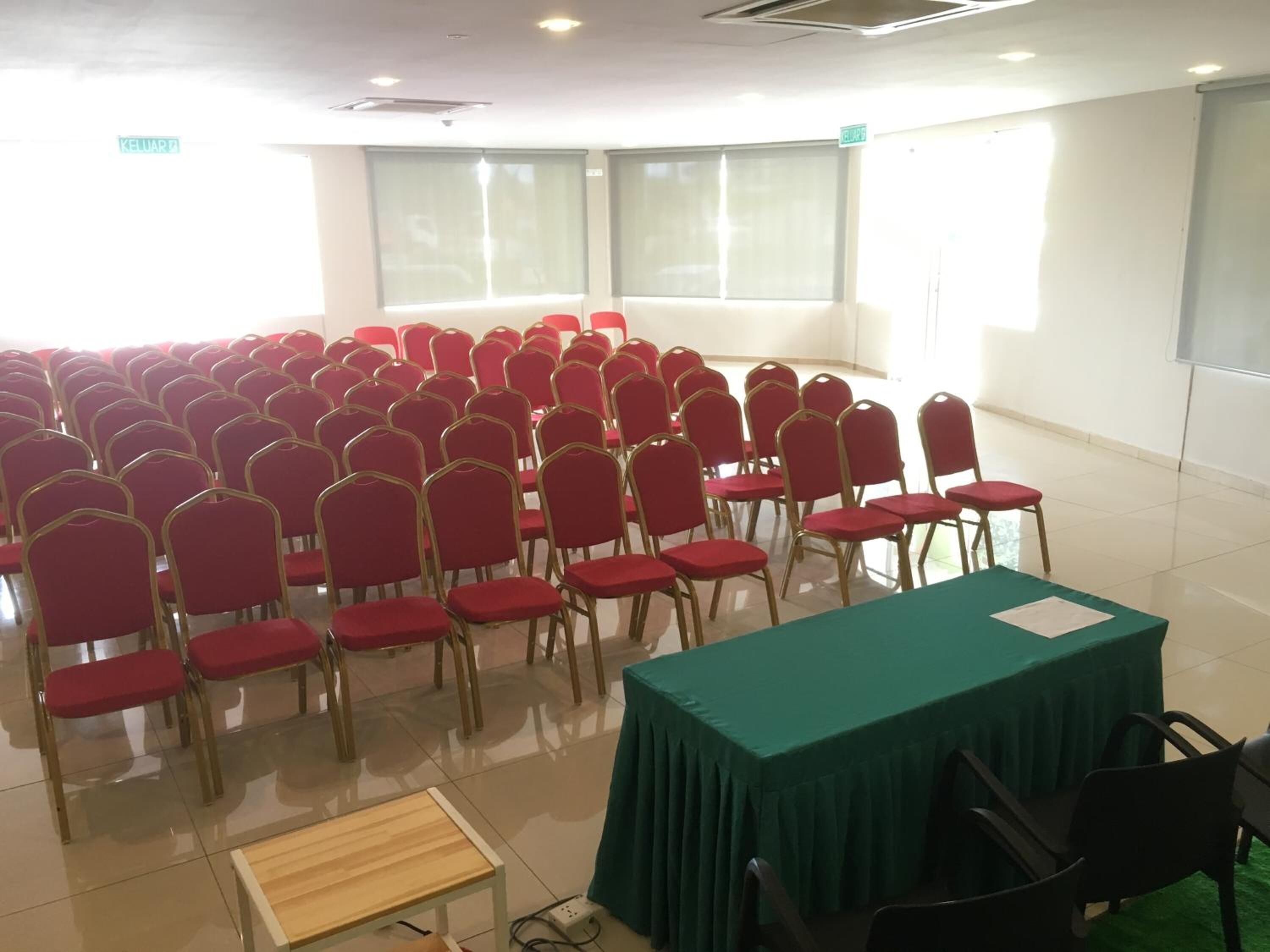 A conference room with rows of red chairs, a green table, and a projector screen.
