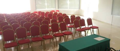 A conference room with rows of red chairs, a green table, and a projector screen.