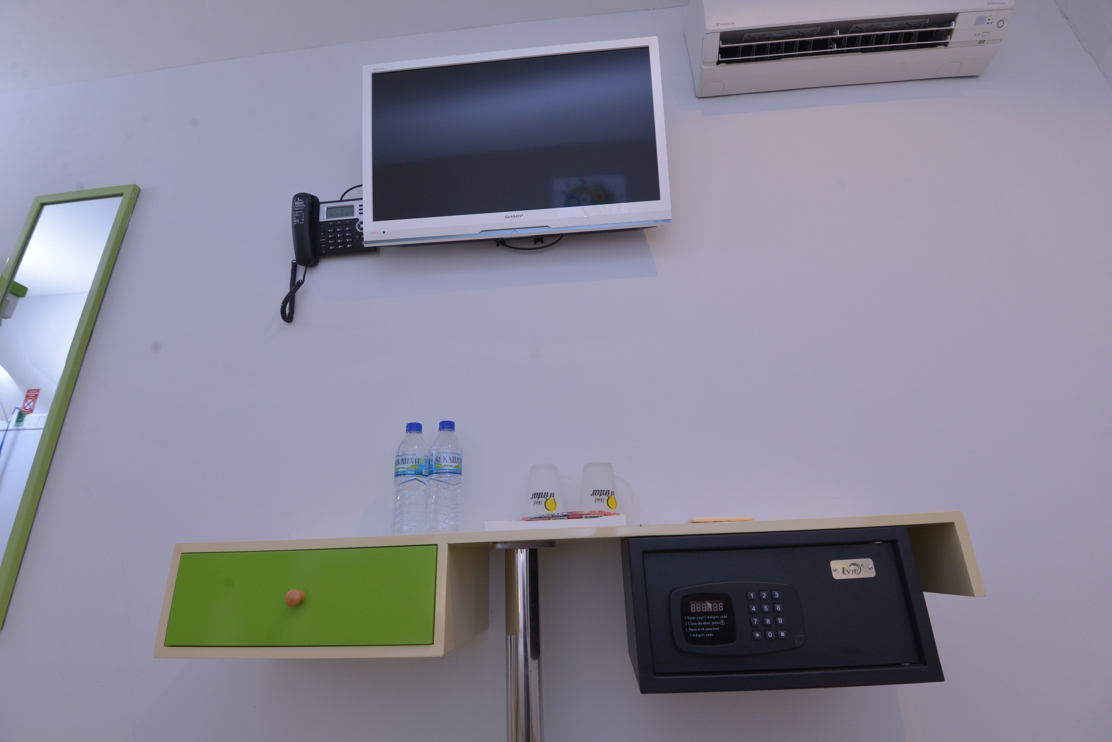 A room with a desk, a phone, a monitor, and an air conditioner.