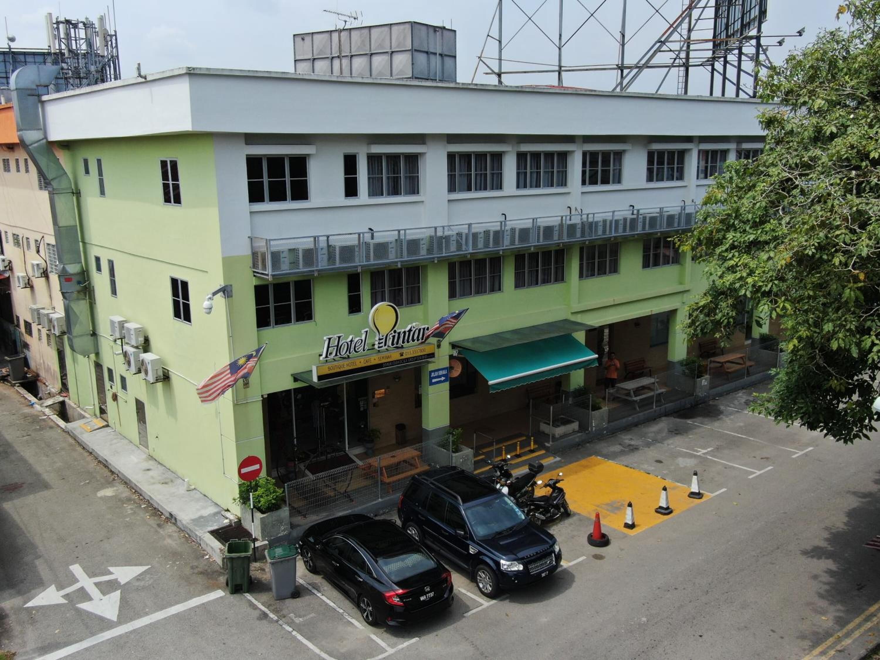 A building with a sign reading "Hotel Intanar" and a green awning. There are parked cars and a yellow parking space marked with cones.