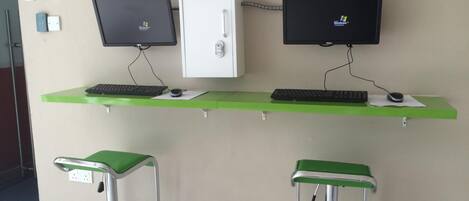 A desk with two monitors, a keyboard, and a mouse on a green desk. There are two green stools with metal frames.