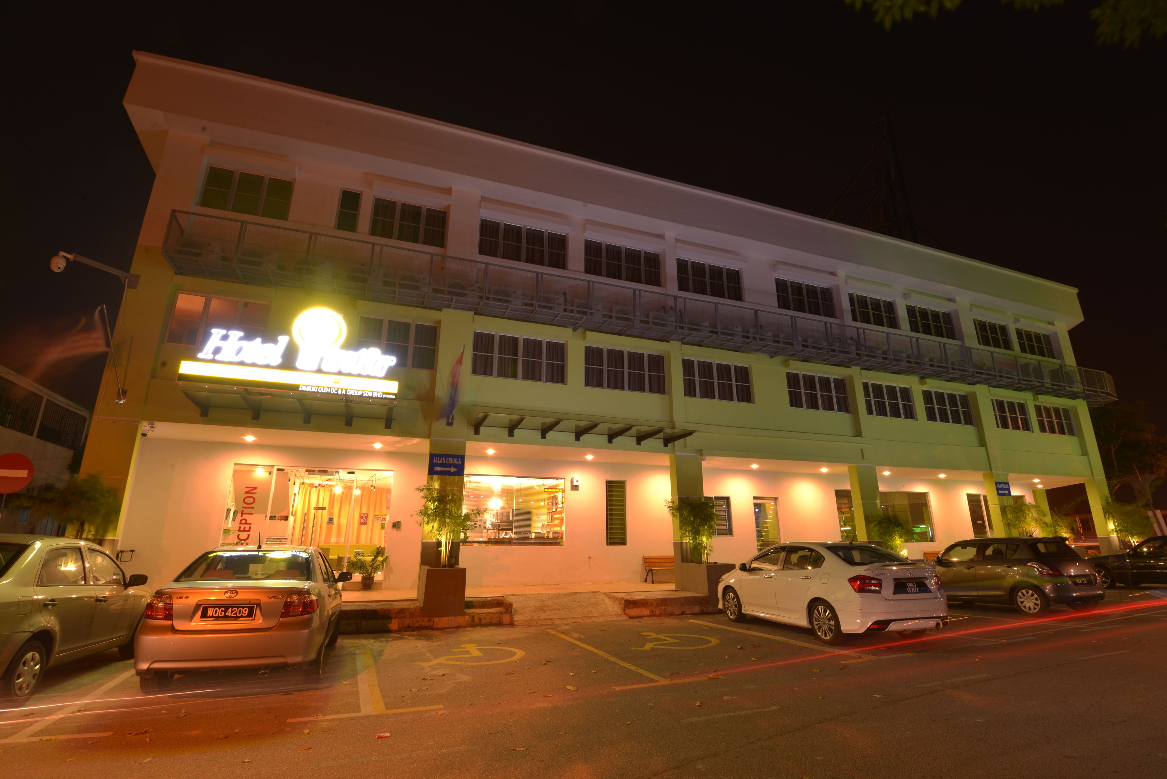 A hotel with a two-story structure, a reception area, and a parking lot with several cars.