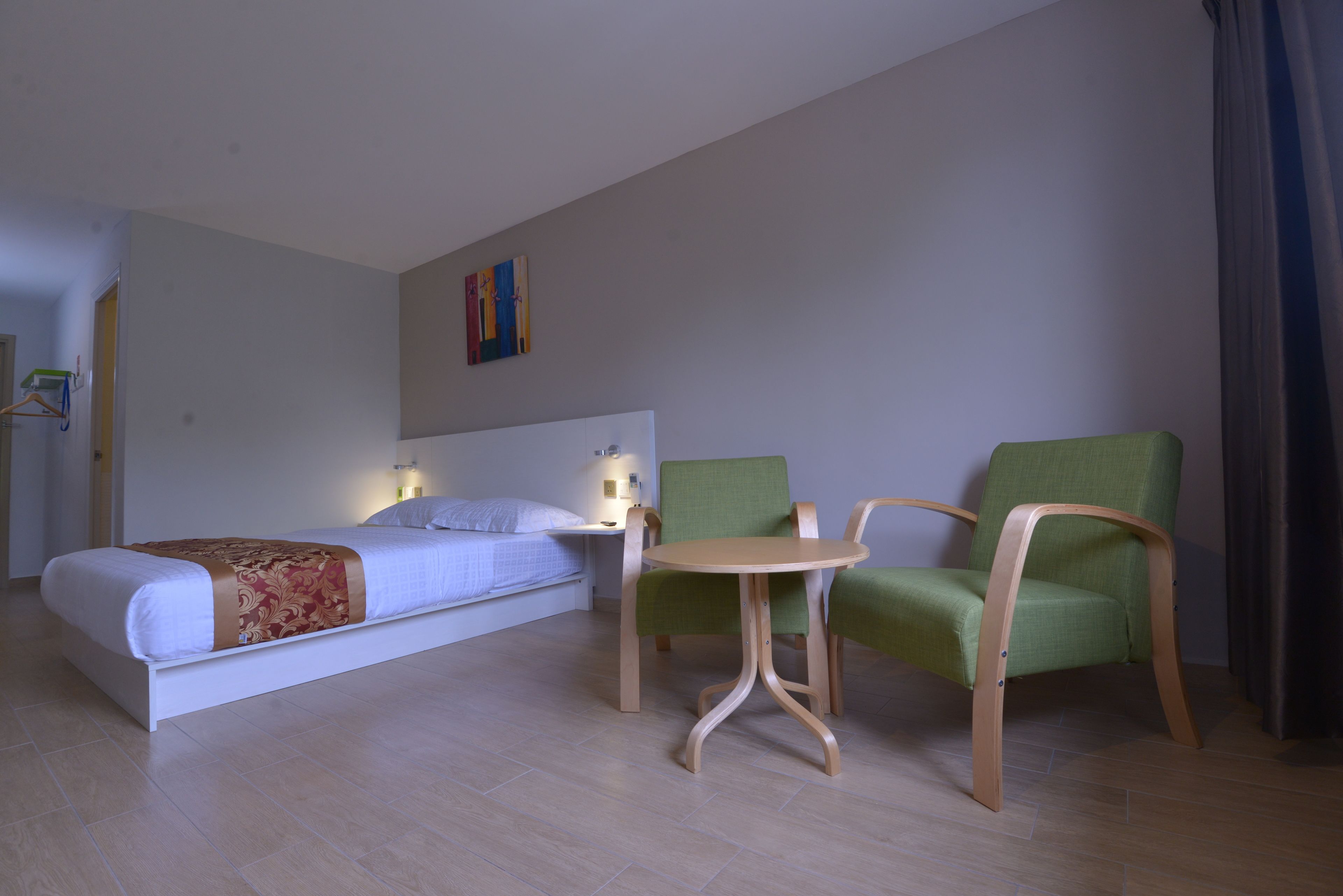 Una camera d'albergo con un letto, due poltrone, un tavolino e un quadro appeso al muro.