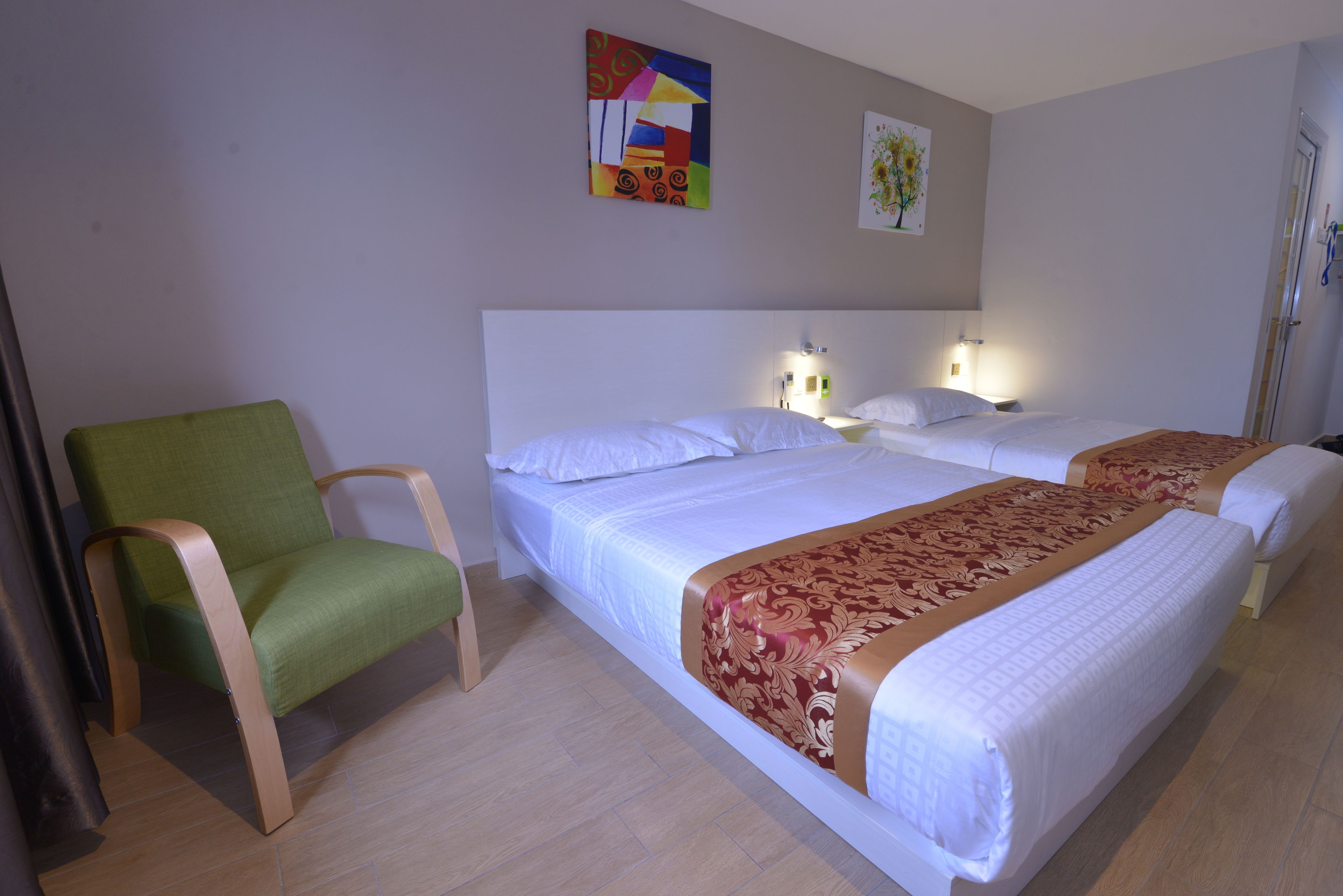 Habitación de hotel con dos camas, una silla verde y obras de arte en las paredes.