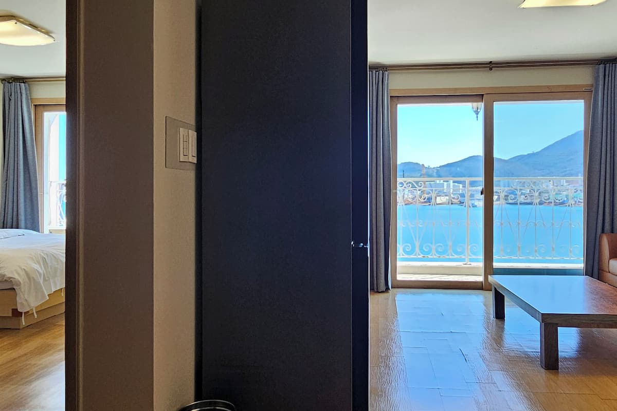 Habitación de hotel con cama, sofá, mesa y balcón con vistas al mar y las montañas.