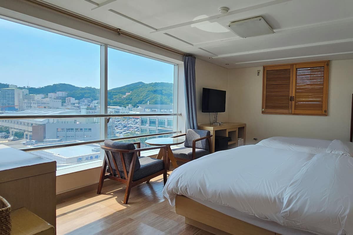 Habitación de hotel con un ventanal grande, una cama, un escritorio y una silla.
