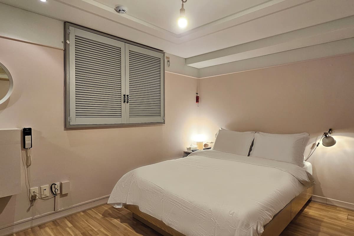 Un dormitorio con cama, lámparas de noche, un espejo redondo, armario y ventana con contraventanas.