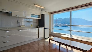 A modern kitchen with white cabinets, a wooden bench, and a large window offering a view of the sea and mountains. - Hansan Hotel (Tongyeong)
