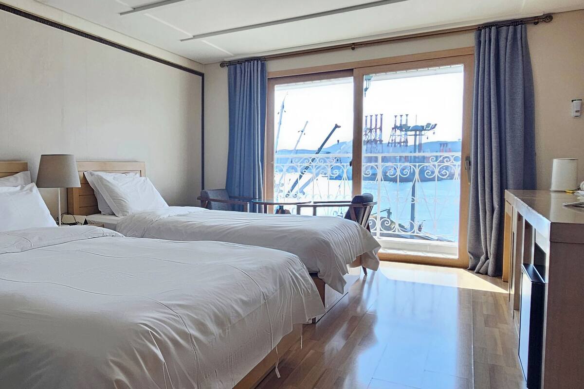 Habitación de hotel con dos camas, un escritorio y vistas al balcón.