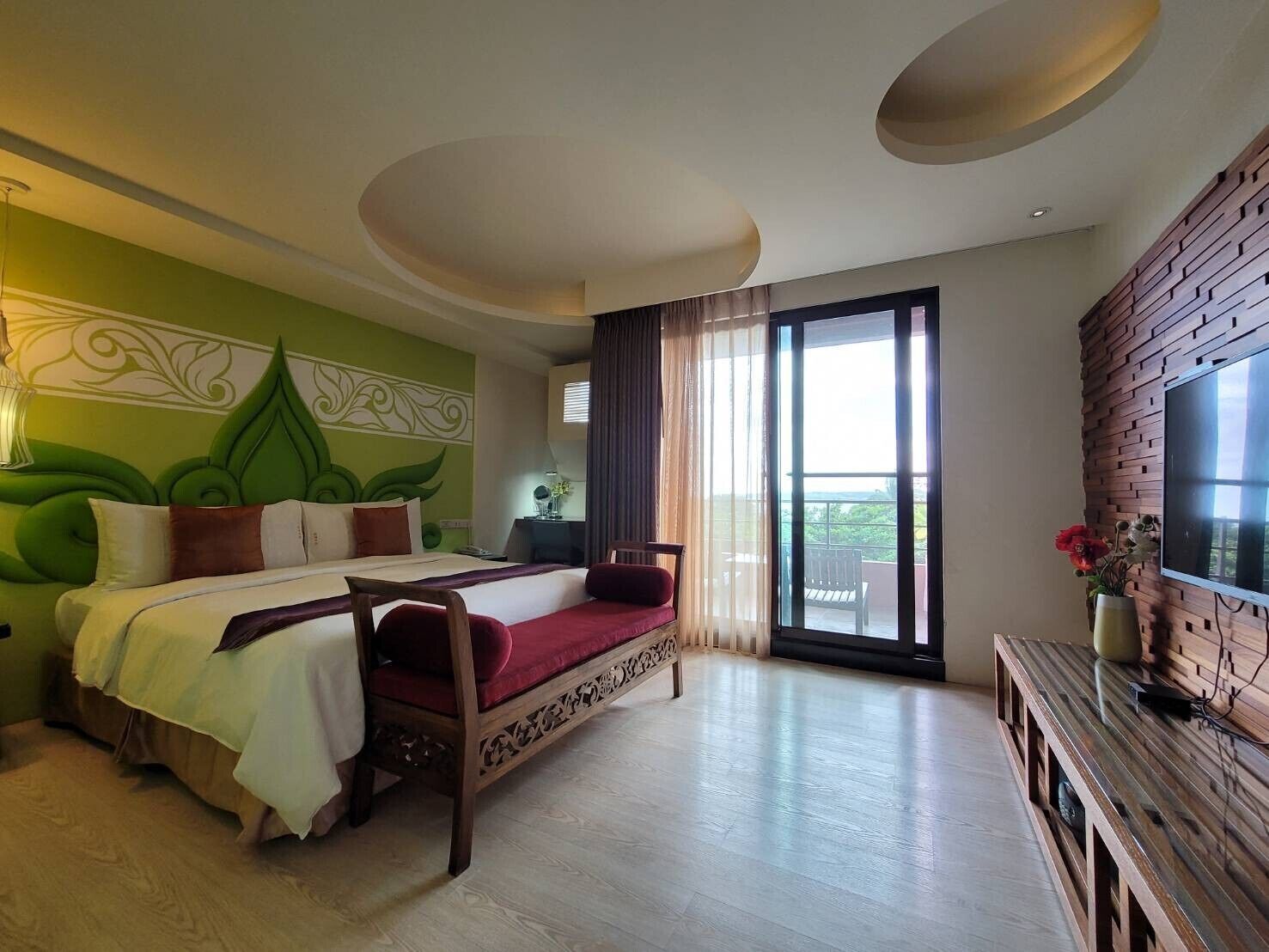A hotel room with a bed, a desk, a TV, and a balcony with a view.