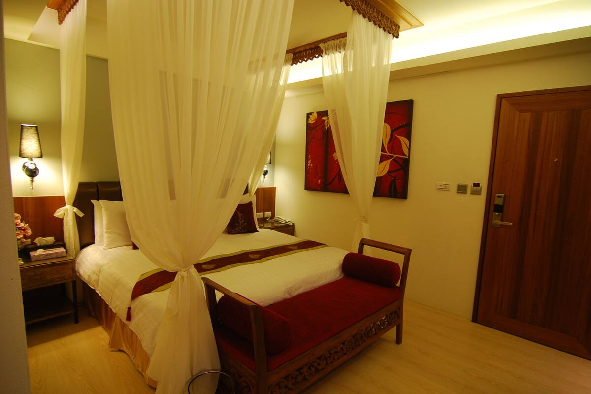 A bedroom with a bed, bedside tables, a nightstand, a wooden door, and a wall with a painting.