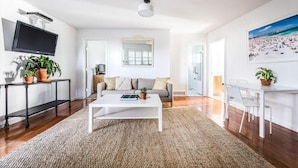 Un salon moderne avec un canapé blanc, une table basse et un téléviseur fixé au mur. On y trouve également des plantes en pot et un tableau accroché au mur.