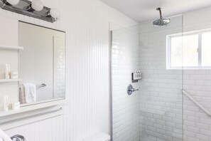 A modern bathroom with a glass shower enclosure, white tiled walls, a large mirror, and a window.