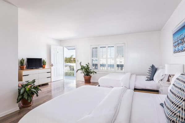 A modern hotel room with a large bed, a TV, a desk, and potted plants.