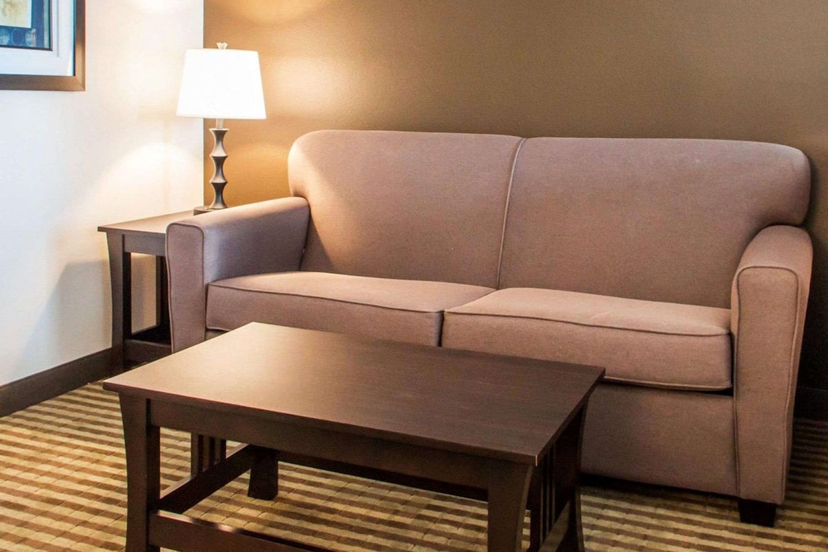 A modern hotel room with a beige sofa, a wooden coffee table, and a lamp on a side table.
