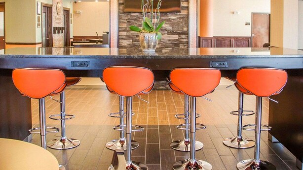 A bar area with four orange bar stools, a stone accent wall, and a vase with white flowers. - Comfort Inn & Suites Woodward (Woodward)