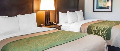 A hotel room with two beds, a nightstand with a lamp, a telephone, and a framed picture on the wall.