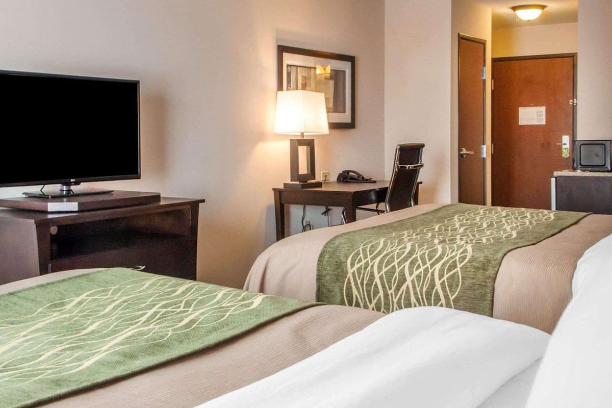 A hotel room with two beds, a desk with a lamp, a television, and a door.