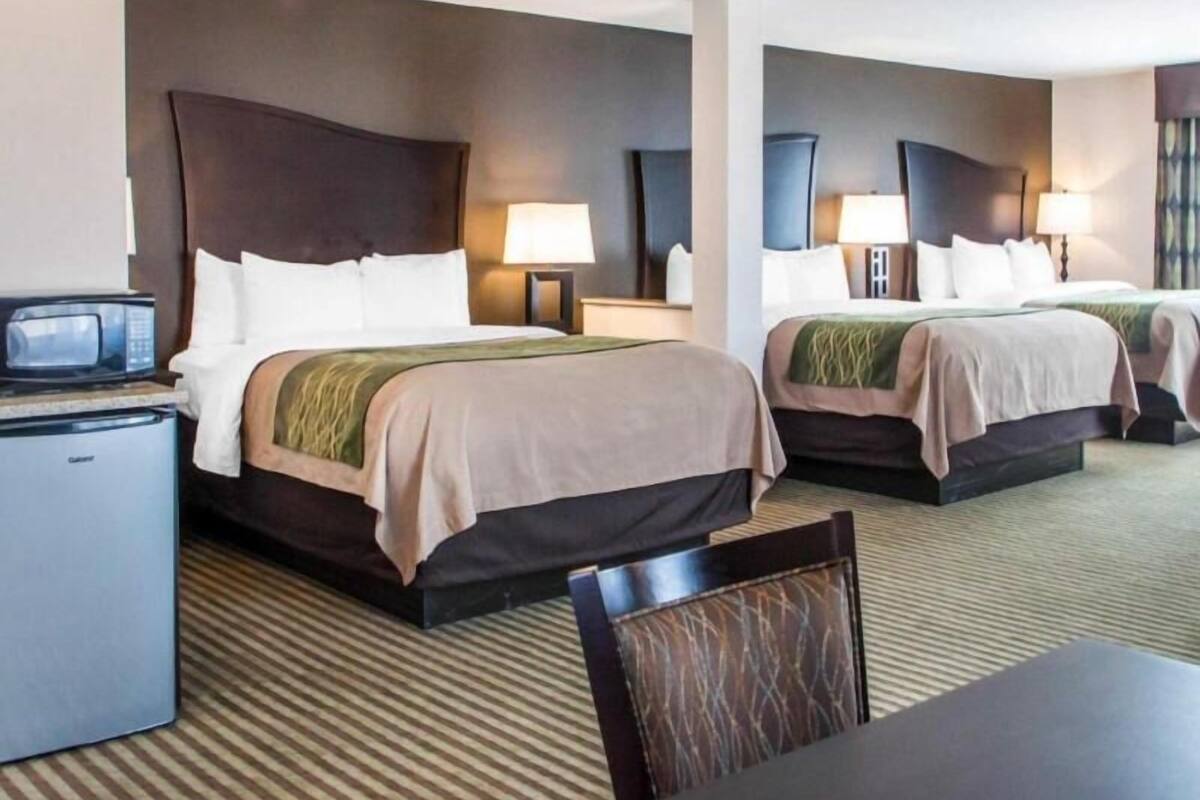 Quarto de hotel com duas camas, uma escrivaninha, um micro-ondas e uma cadeira.
